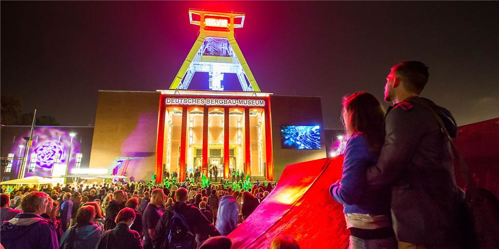 Extraschicht 2022: Zehn Spielorte, die Sie wirklich sehen müssen Besucher betrachten das erleuchtete Bergbaumuseum in Bochum.
