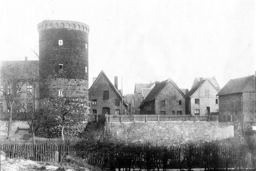 Das Bild aus der Zeit um 1910 zeigt den Blick zwischen den Häusern von Anton Droste (links) und Schuhmacher Bickhofe (rechts) hindurch in den Gantepoth. Einen Durchstich, der über den alten Stadtwall und -graben auf die Rochfordstraße hinausführte, gab es zur damaligen Zeit noch nicht. Von dem Törchen rechts neben dem Siebenteufelsturm führte eine schmale Treppe hinunter auf den im früheren Stadtgraben liegenden Gartenweg. Das an der rechten Bildseite zu sehende Fachwerkhaus, an der Ecke des heutigen Kärntner Platzes, wurde erst 1952 abgerissen.