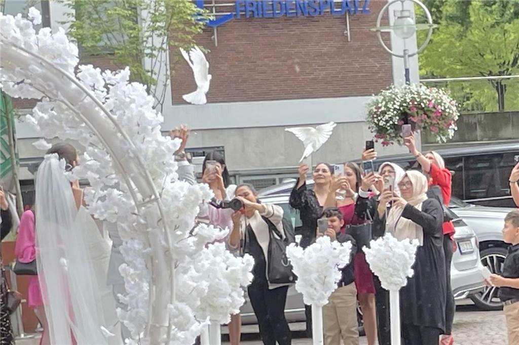 Antrag vor Apple Store: Harun und Sümeyye haben in Dortmund geheiratet Weiße Tauben fliegen in die Luft. Die Hochzeitsgesellschaft schaut den Tieren hinterher und filmen mit ihren Handys.