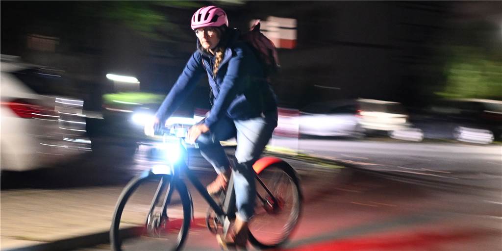 Eine Frau fährt mit ihrem Fahrrad am frühen Morgen über eine Straße.