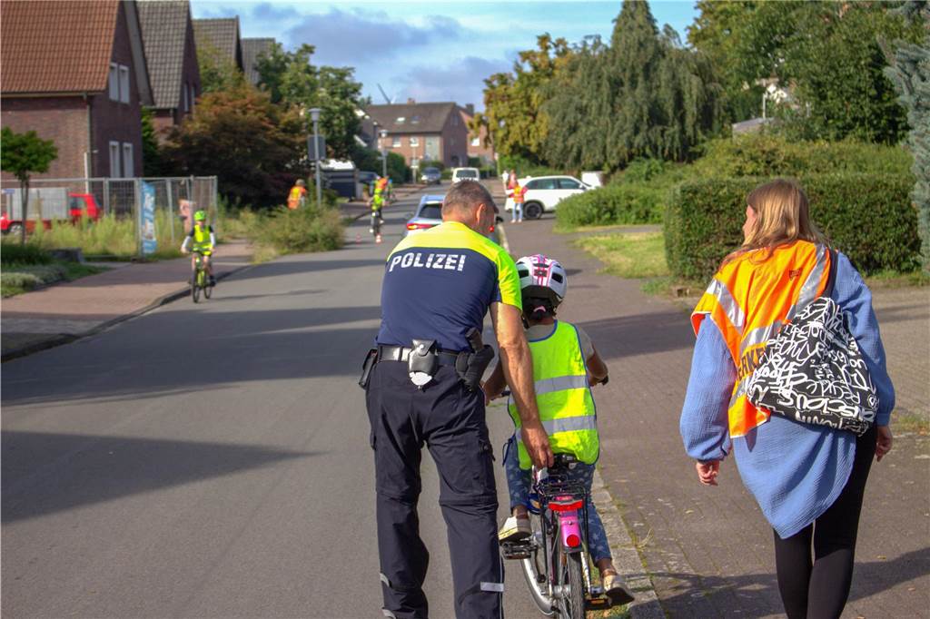 Verkehrssicherheit an Schulen: Raser bekommen selbst gemalten Denkzettel Polizist hilft Kind auf dem Fahrrad.