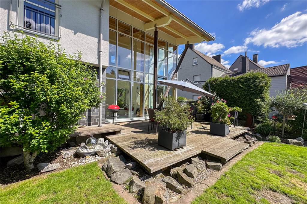 Extravagante Immobilien: Fußbodenheizung im Keller oder hohe Fenster Foto eines Hauses vom Garten aus. Die Sonne scheint, die Terrasse ist aus Holz und ein Sonnenschirm ist aufgespannt. Die Fenster sind haushoch.