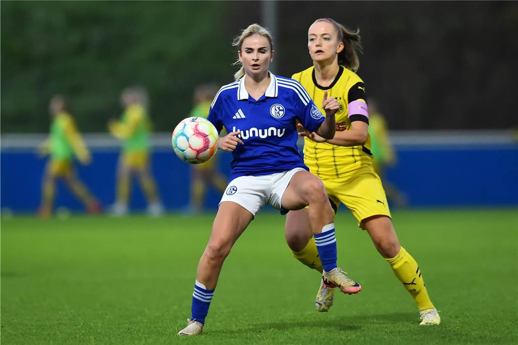 Eine Spielerin von Schalke schirmt den Ball vor einer BVB-Spielerin ab.