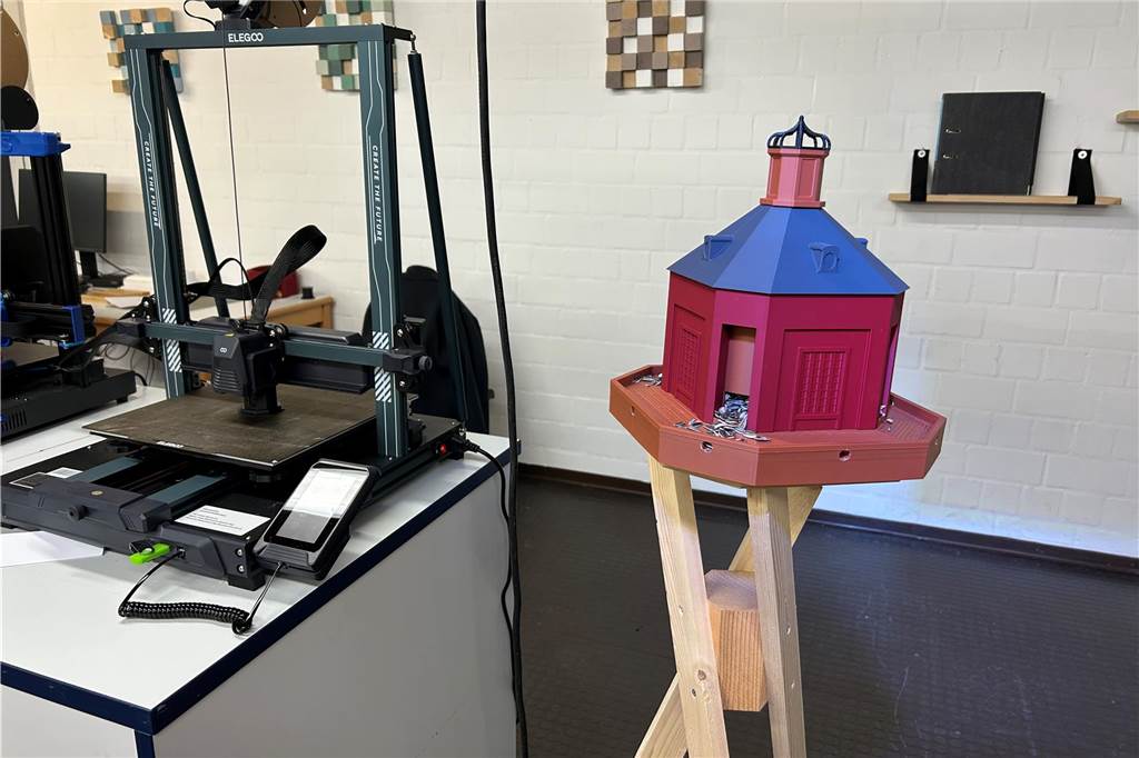 Ein Vogelhäuschen im Stile des Hochzeitstürmchens, daneben ein 3D-Drucker