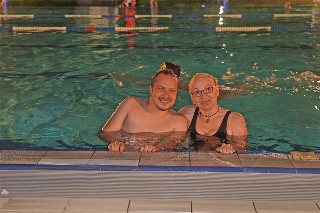 Fotos vom Nachtschwimmen 2024 im Freibad Castrop-Rauxel bei Regen. Besucher schwimmen unter freiem Himmel bei Fackelschein am Abend. Entspannte Atmosphäre und kulinarisches Angebot. 
