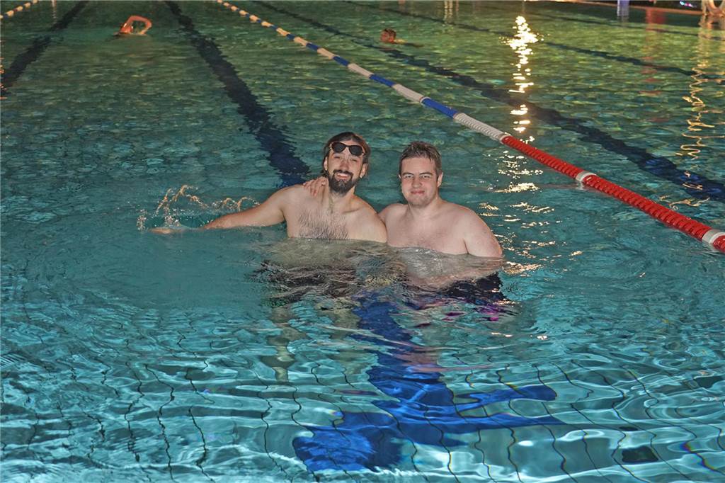 Fotos vom Nachtschwimmen 2024 im Freibad Castrop-Rauxel bei Regen. Besucher schwimmen unter freiem Himmel bei Fackelschein am Abend. Entspannte Atmosphäre und kulinarisches Angebot. 
