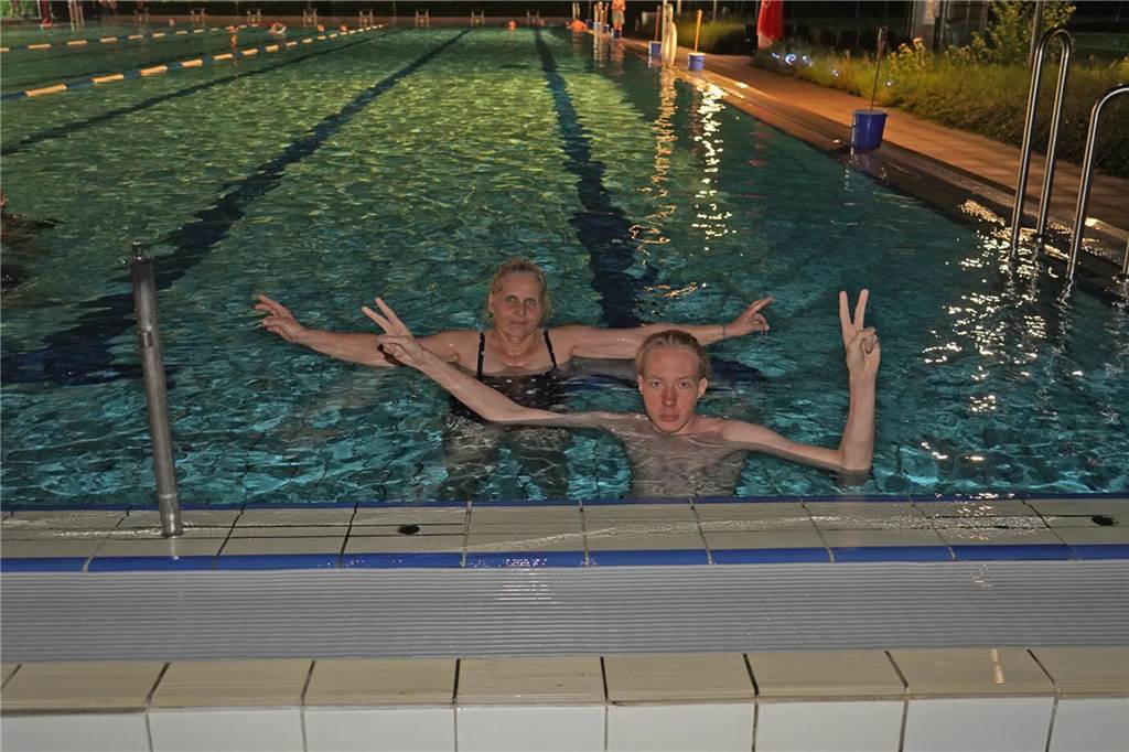 Fotos vom Nachtschwimmen 2024 im Freibad Castrop-Rauxel bei Regen. Besucher schwimmen unter freiem Himmel bei Fackelschein am Abend. Entspannte Atmosphäre und kulinarisches Angebot. 
