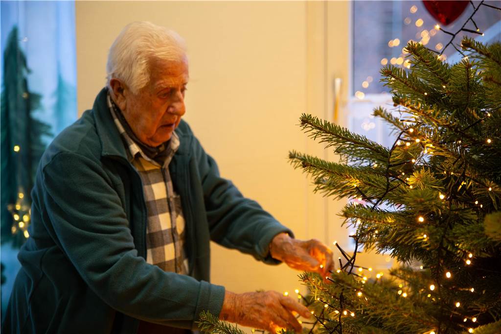 Adventszeit: Besinnliches Weihnachtsfest im Kirchhellener Seniorenheim Ein Mann schmückt den Weihnachtsbaum mit einer Lichterkette.