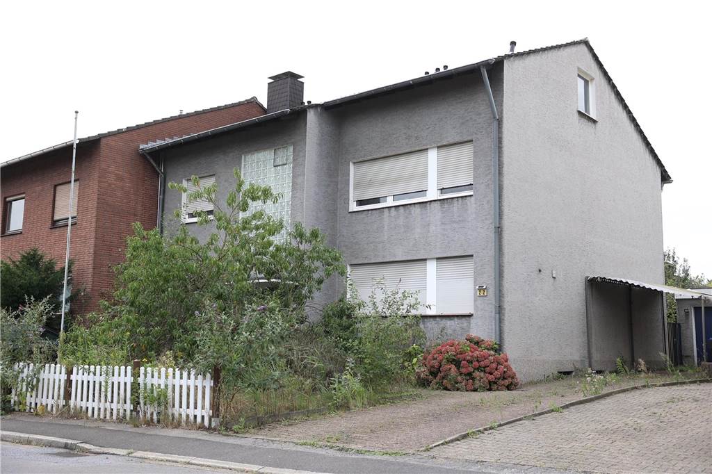 Vor dem grauen Zweifamilienhaus in Lünen wuchern Sträucher.