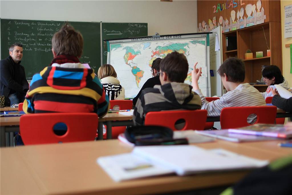 Zwei Heizlüfter für die Gesamtschule: Dauerhafte Lösung fehlt noch Kinder einer Schule sitzen im Unterricht. Ein Lehrer steht vorne an der Tafel.