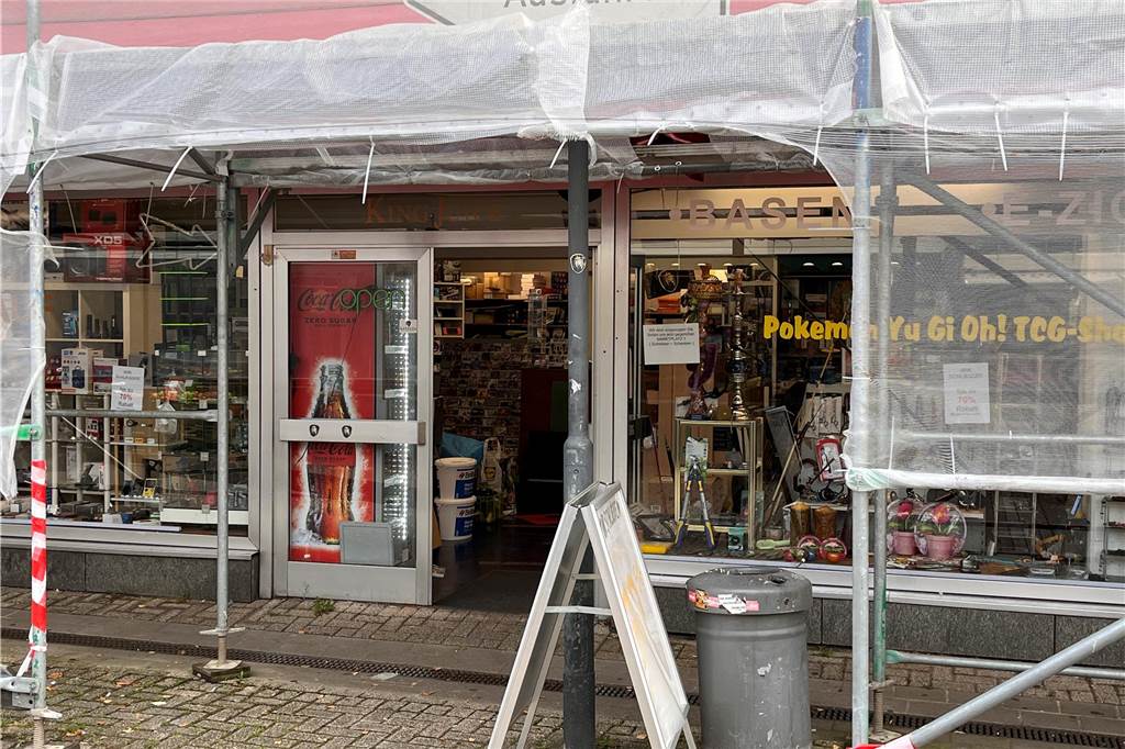 Baugerüst vor Eingangsbereich eines Geschäftslokals, ein Aufsteller steht noch davor, neben einer grauen Mülltonne.