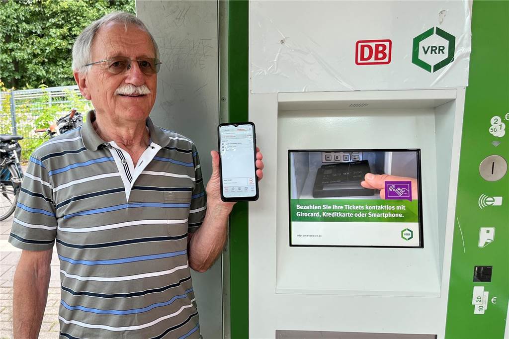 E-Tarif statt Abo: Detlef Oertel (79) entdeckt das 49-Euro-Schlupfloch Mann steht neben einen Ticket-Automaten und hält in der linken Hand ein Smartphone.