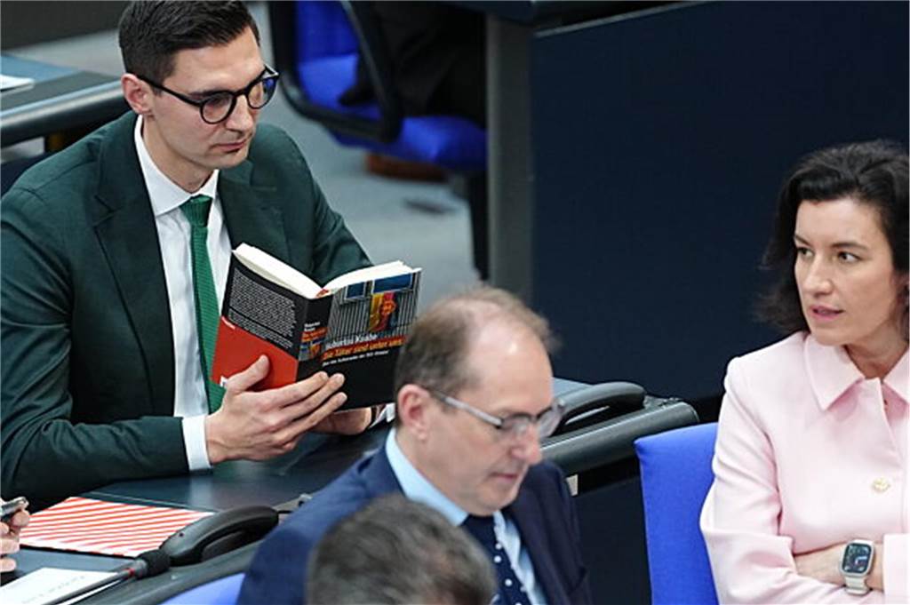 AfD rückt laut Umfrage näher an Union heran: Scholz erhält Entlassungsurkunde - Newsblog Der Abgeordnete Sepp Müller (l, CDU) hält das Buch "Die Täter sind unter uns" während der Rede von Alterspräsident Gysi (Die Linke).