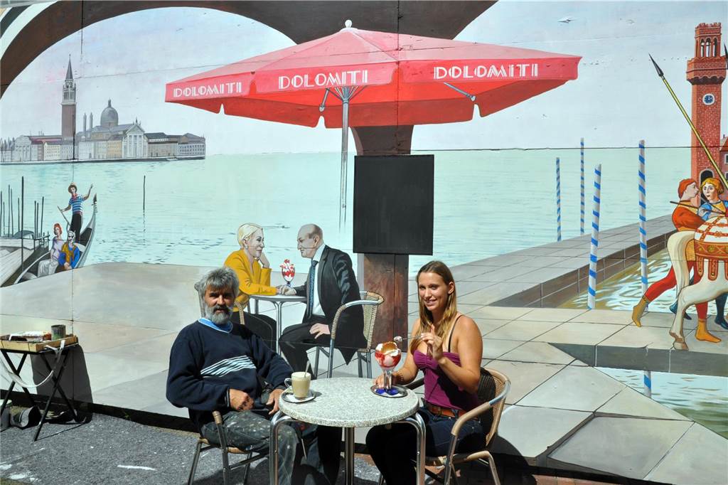Aufzug-Einbau am Hauptbahnhof lässt Wandbild mit Filmhelden verblassen Künstler mit Lünerin am Tisch vor dem bemalten Bauzaun