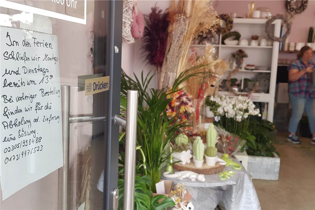 Eingang des Blumenladens Pusteblume in der Altstadt von Castrop-Rauxel. Man sieht ein Schild mit den geänderten Öffnungszeiten. Im Hintergrund arbeitet Claudia Jung allein.