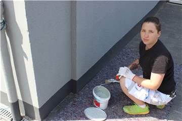 Der Boden ist mit Malervlies geschützt, die Arbeit kann beginnen: Janine Kolmanic ist bereit, den Sockel der Fassade zu streichen. Foto: Starb