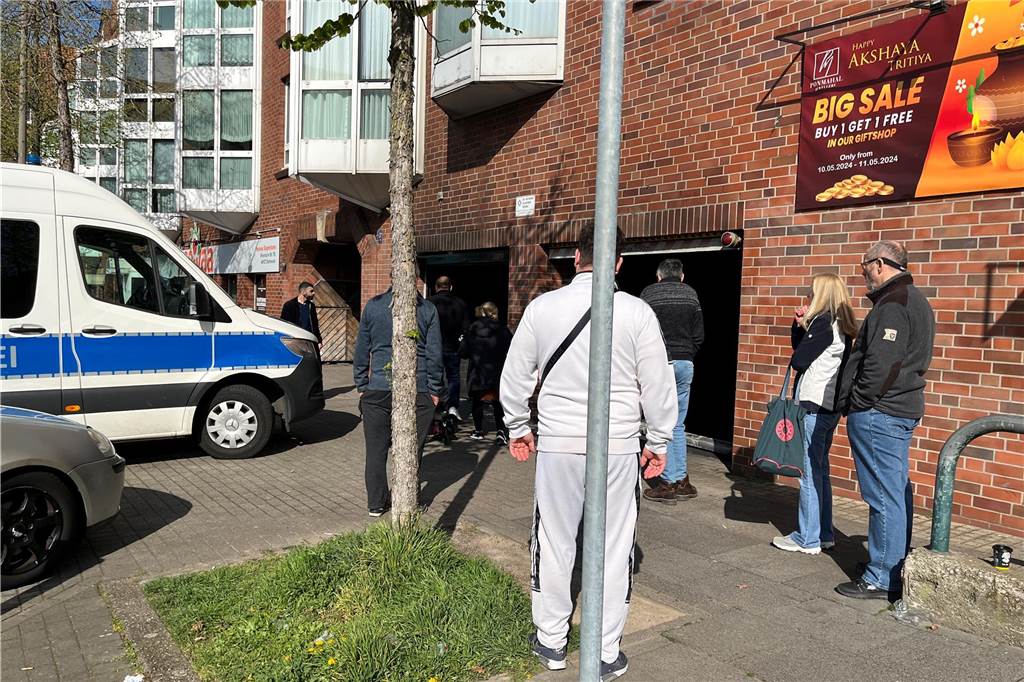 Anwohner stehen vor der Tiefgarage, in der es gebrannt hatte. Davor steht auch ein Polizeifahrzeug.
