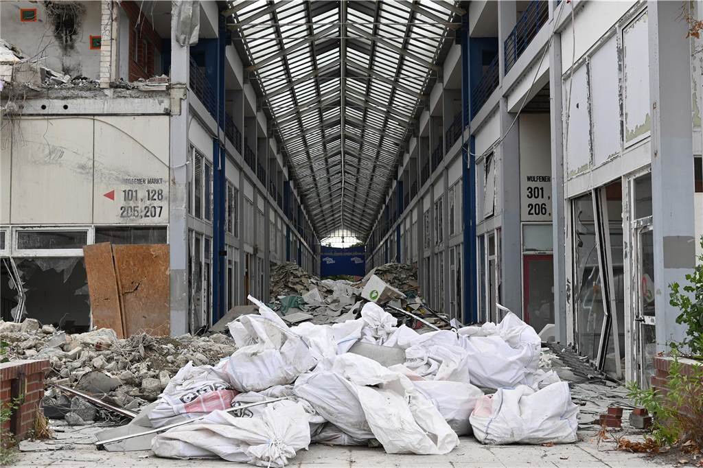 Der erste Flügel, vom Marktplatz aus gesehen links, ist bereits komplett abgerissen. Hier werden nur noch die Baustoffe getrennt. Auf der anderen Seite zerlegen die Bagger die einzelnen Wohnungen, Stockwerk für Stockwerk. Auch hier nähert man sich rasant der mittleren ehemaligen Einkaufsmeile.