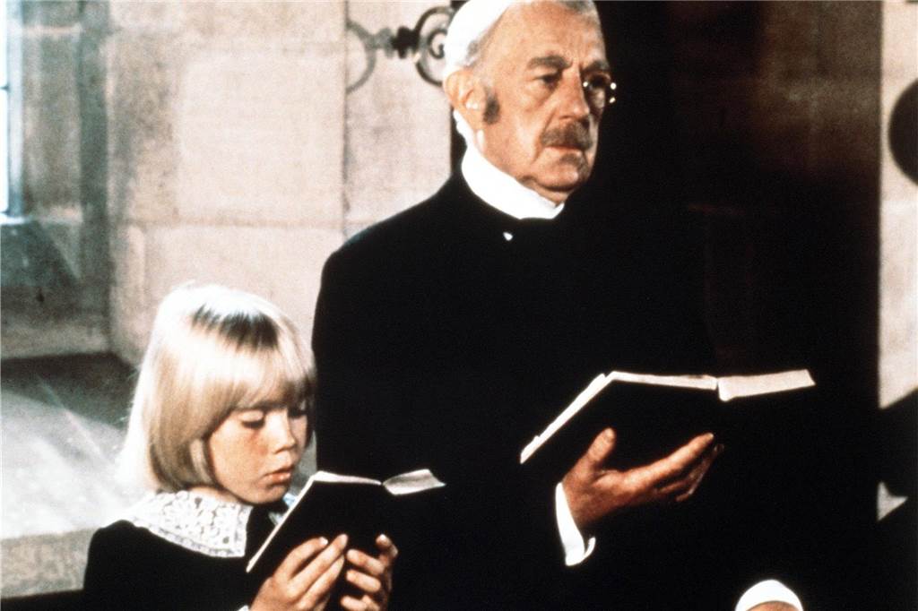 Schauspieler Alec Guinness hält ein Gesangbuch.