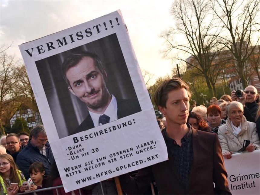 Böhmermann mit Kritik an Kanzlerin zurück Der Schauspieler Max Mauff hält vor der Verleihung der Grimmepreise eine Plakat mit der Aufschrift «Vermisst», das auf die Abwesenheit des Satirikers Jan Böhmermann hinweist. Foto: Henning Kaiser
