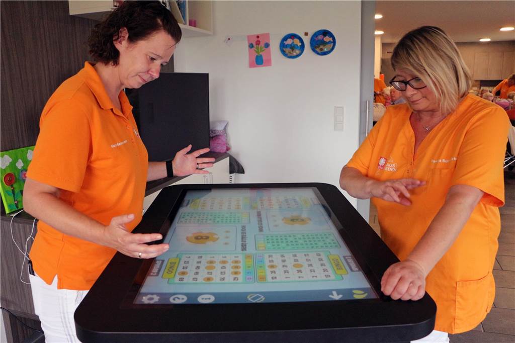 Digitaler Weg in der Tagespflege: Care Table bereichert den Pflegealltag Der Tisch kann auch von mehreren Nutzern gleichzeitig genutzt werden. Hier demonstrieren Karin Bennemann (l.) und Daniela Büter-Liebner vom Team eine Bingo-Runde.