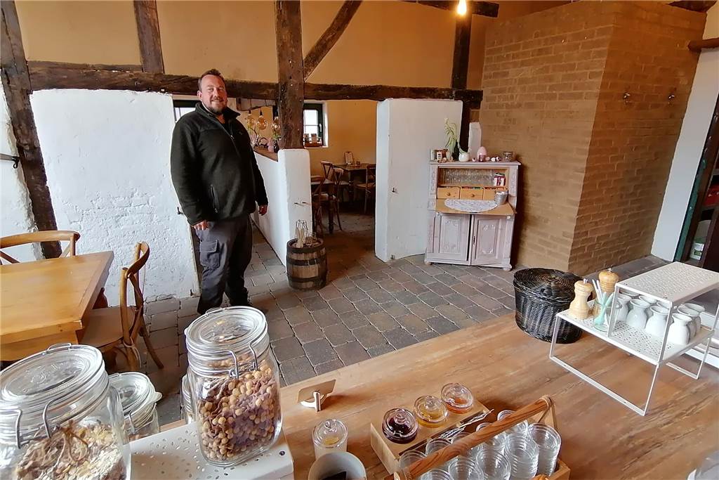 Hof Menken: Nasser Boden behindert frühen Start in die Spargel-Saison Jan Menken im umgebauten Stall des Hofes. Im Vordergrund das Buffet, im Hintergrund, hinter einer Fachwerkwand sind Sitzgelegenheiten.
