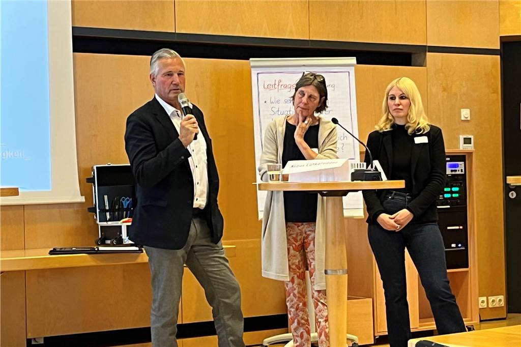 Soziale Projekte für angespannten Wohnungsmarkt: „Wir sind Vermittler“ Mann steht mit einem Mikrofon neben zwei Frauen, die an einem Stehtisch stehen.