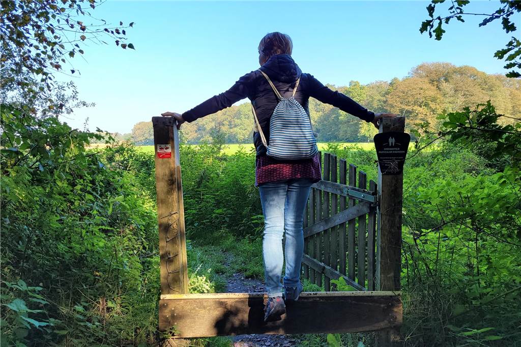 Über Stock und Stein auf dem Holzschuhwege in Woold Eine Wanderin geht durch ein Gatter.