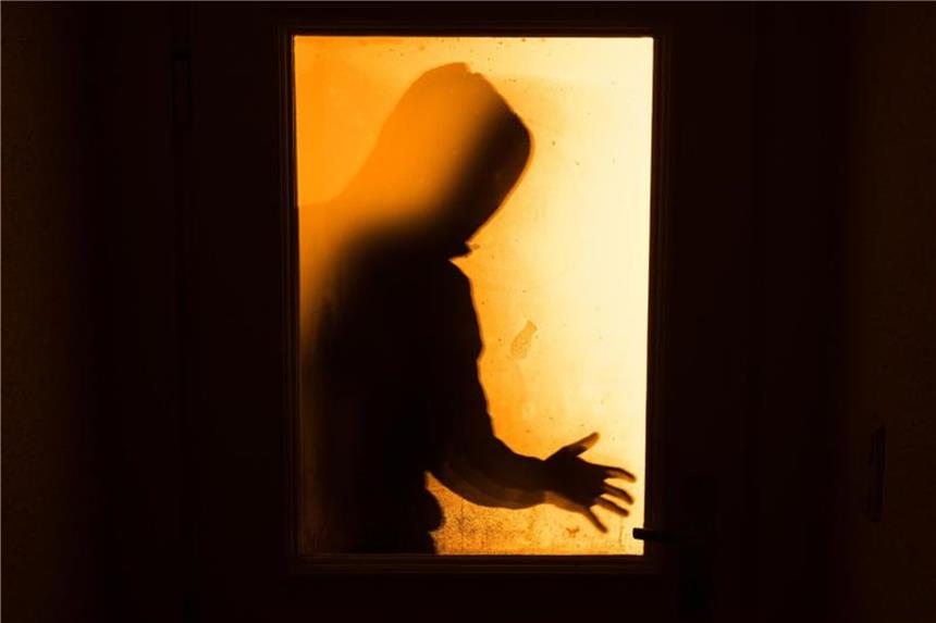 Der Schatten eines Mannes ist hinter einer gläsernen Wohnungstür zu sehen. Foto: Nicolas Armer/Archiv