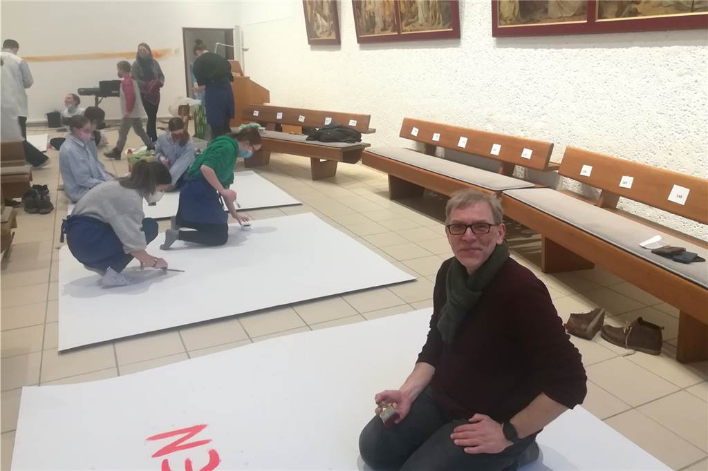 Kinder malen den Frieden: „Meine Oma hat Angst vor einem neuen Krieg“ Diakon Michael Reckmann vor einer Pappe, die er bemalt.