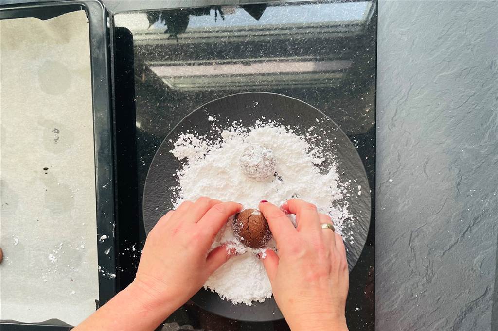 So gelingen die festlichen Schokoflocken-Plätzchen Die abgekühlten Schokoflocken-Plätzchen in Puderzucker wälzen.