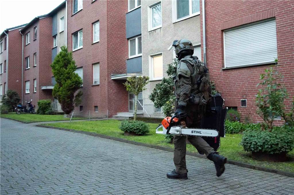 Ein SEK-Beamter geht an einem Mehrfamilienhaus in Datteln vorbei, während er eine Kettensäge trägt.