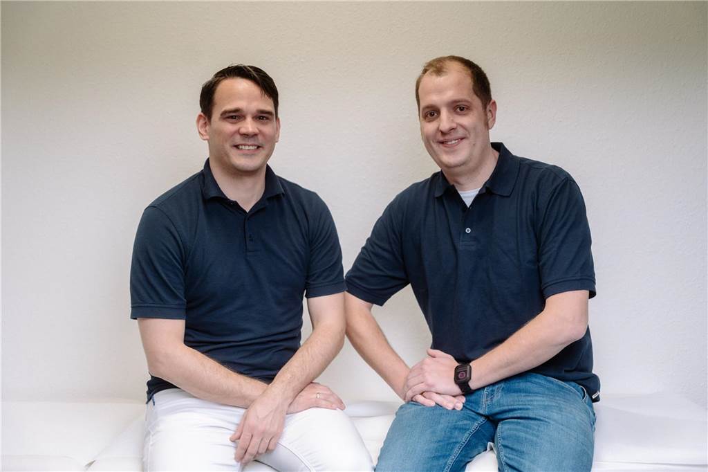 Praxisübernahme und Zuwachs in Ahaus: Aus Dr. Rotering wird Ärzte-Trio Christopher Rotering und Sebastian Torka sitzen auf einer Patientenliege.