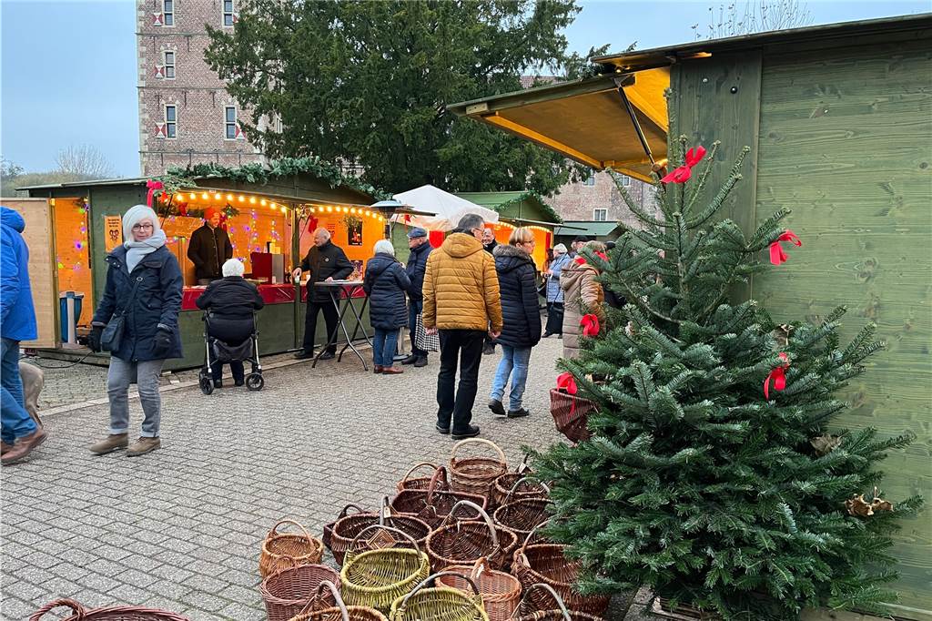 Menschen schlendern über den Raesfelder Adventsmarkt. Im Vordergrund steht ein Tannenbaum.