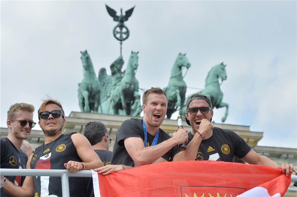 Sorgen um Kevin Großkreutz vor Kracher-Duell gegen Brünninghausen: „Wird ein heißes Spiel“ Die deutschen Nationalspieler Andre Schürrle (von links nach rechts), Mario Götze, Kevin Großkreutz und Lukas Podolski jubeln am 15.07.2014 vor dem Brandenburger Tor in Berlin den Fans zu.