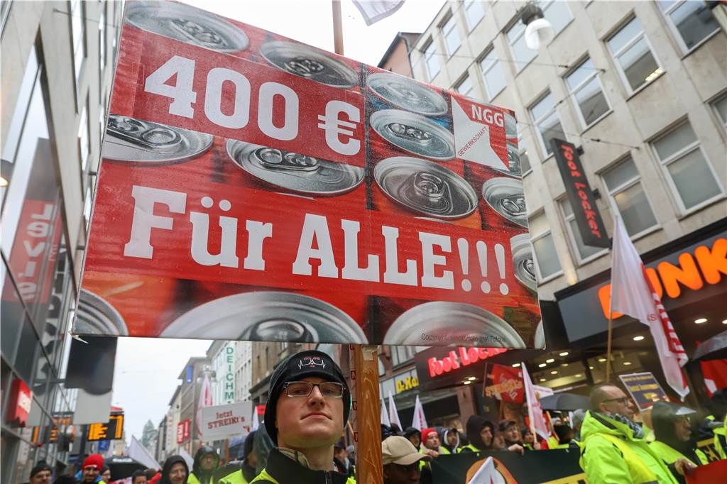 Hunderte Beschäftigte von Coca-Cola haben in Dortmund gestreikt Ein streikender Beschäftigter von Coca-Cola hält ein Schild mit der Forderung "400 Euro für alle".