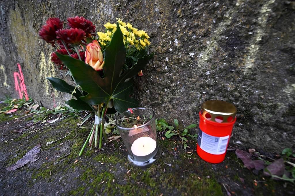 Mann greift Kinder auf Schulweg mit Messer an: Mädchen schwer verletzt Blumen und Kerzen stehen an Markierungen der Spurensicherung der Polizei an einem Tatort auf einem Weg.