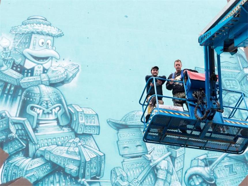 Die Graffiti-Künstler Loomit (l) und WonABC auf einer Hebebühne vor ihrem Graffiti-Kunstwerk in München. Foto: Alexander Heinl