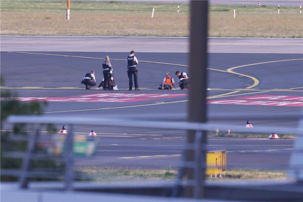 Auswirkungen der Klimakrise auf NRW: Hitze, Flut und gesundheitliche Folgen Polizisten stehen auf dem Flugfeld und versuchen Aktivisten der Gruppe Letzte Generation am Flughafen vom Asphalt zu lösen, nachdem sie sich festgeklebt haben.