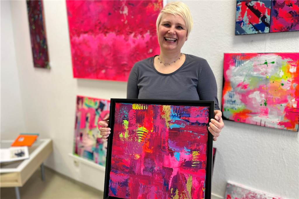 Kunst für jedermann – Galerie Türkis hat seit einem Jahr geöffnet Künstlerin Stefanie Morgenthal hält eines ihrer pinken Bilder in den Händen und lacht.