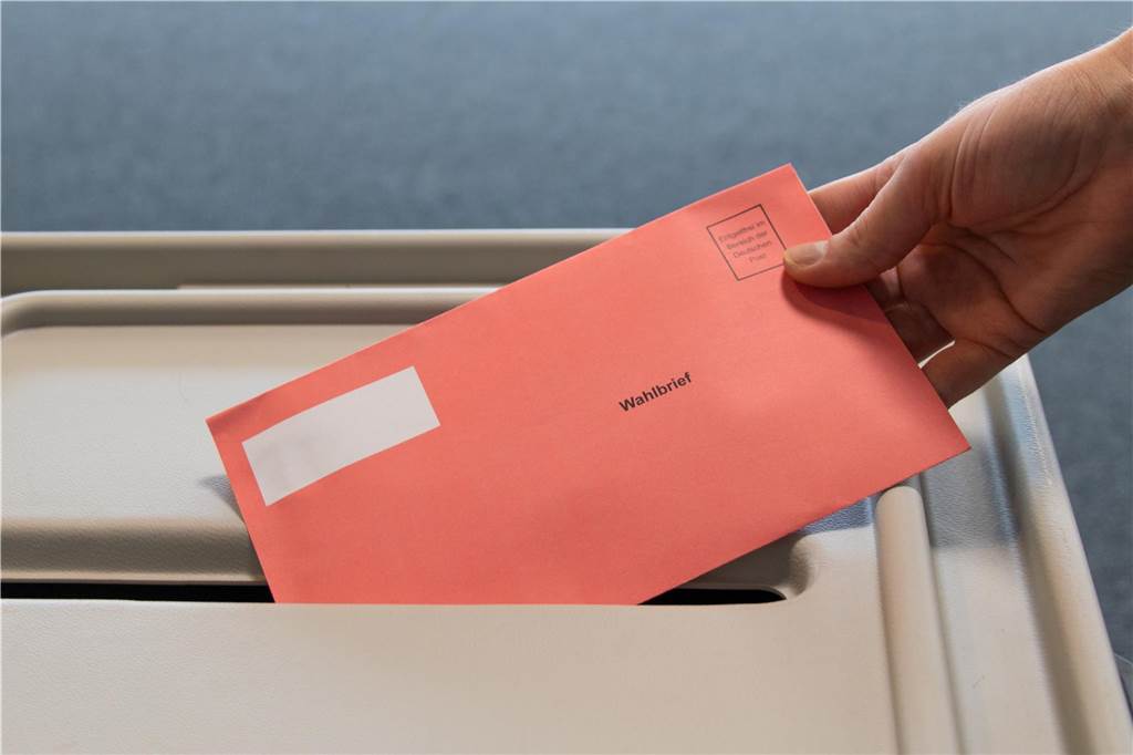 Wahljahr 2025: Für die Bundestagswahl werden Wahlhelfer gesucht Ein roter Wahlbriefumschlag wird in eine Wahlurne geworfen.