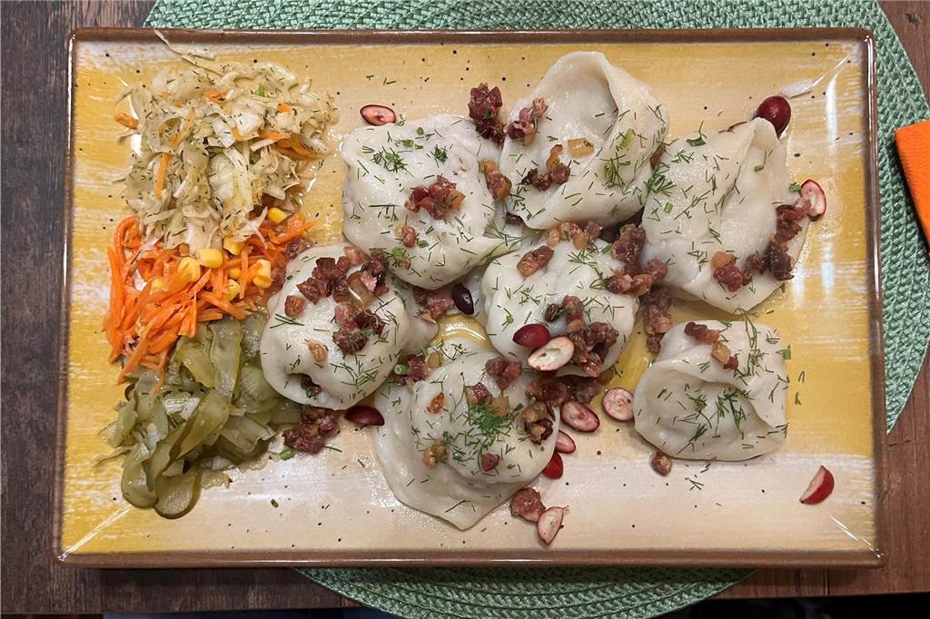 Restaurant „Von Herzen“ im Check: Traditionelle polnische Küche wie bei Mama Ein Teller mit sieben großen Teigtaschen, gefüllt mit Fleisch, Speck und Zwiebeln. Als Beilagen gibt es kalte Salate und Salzgurken.