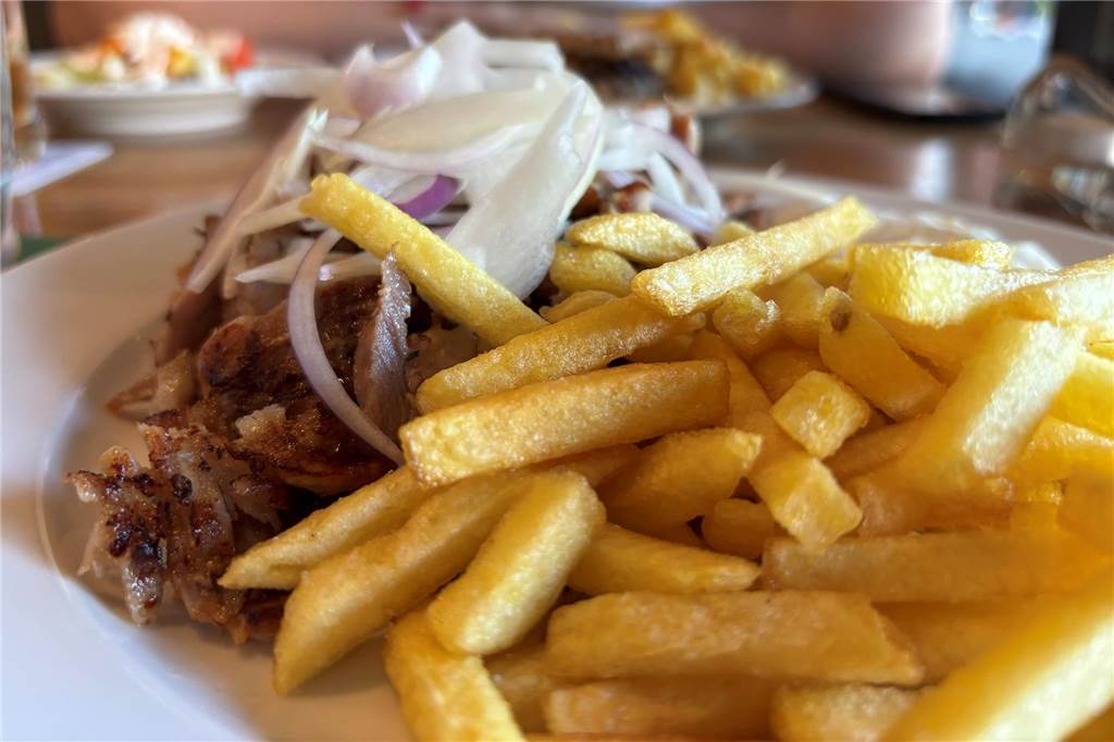 Pommes mit Gyros und Zwiebeln auf einem Teller.