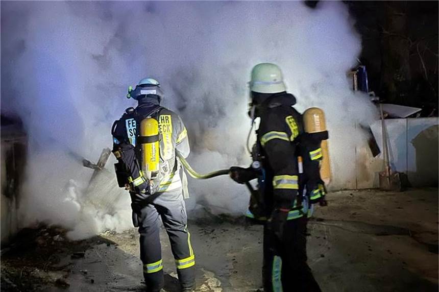 „Gewerbe-/Industriebrand“: Feuerwehreinsatz an der Weseler Straße Zwei Feuerwehrleute löschen einen brennenden Haufen Holz.