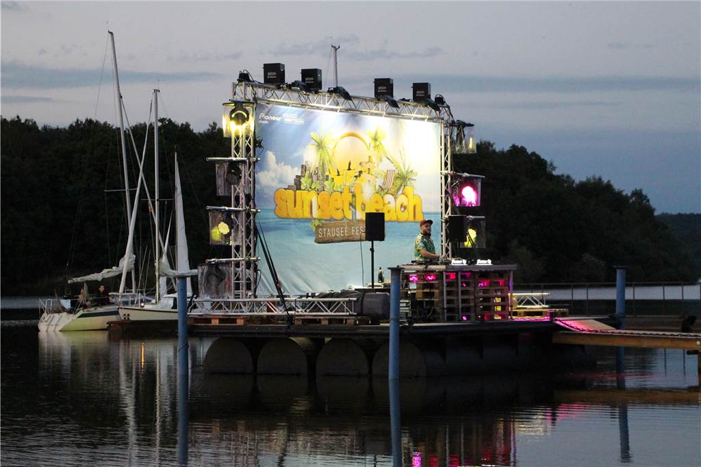 Das erste Sunset Beach Festival: Schlecht-Wetter-Prognosen und Mücken Auf dem Wasser schwimmt eine Bühne mit DJ-Pult.