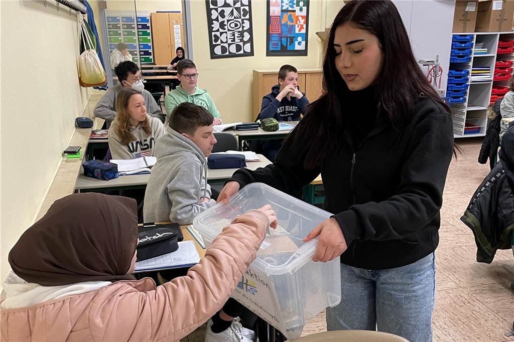 Schüler engagieren sich mit einer Spendenaktion für Erdbebenopfer Eine Schülerin spendet Geld und tut es in eine Spendenbox, die von einer anderen Schülerin gehalten wird.