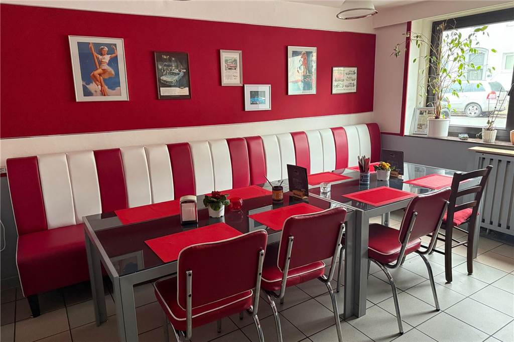 Rot-weiße Tische in einem Restaurant, dazu Stühle, auf denen niemand sitzt.