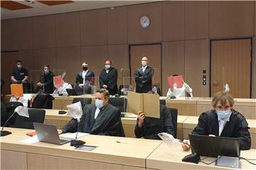Die vier Angeklagten (Gesichter durch Aktendeckel verdeckt) beim Prozessauftakt am 11. November 2021 an der Seite ihrer Verteidiger.
