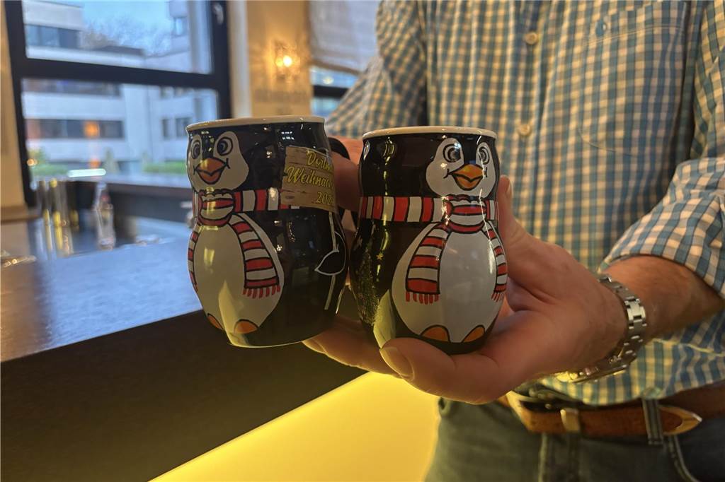 Ein Mann hält zwei Tassen in der Hand. Sie sehen aus wie Pinguine. Es sind die Weihnachtsmarkttassen 2024 für Dortmund.
