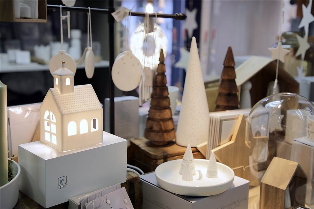 Weihnachtsgeschenke kaufen: Gibt es Trends, auch unter 20 Euro? Weißen Weihnachtshäuser aus Porzellan und Tannenbäume aus Holz stehen bin einem Deko Geschäft.